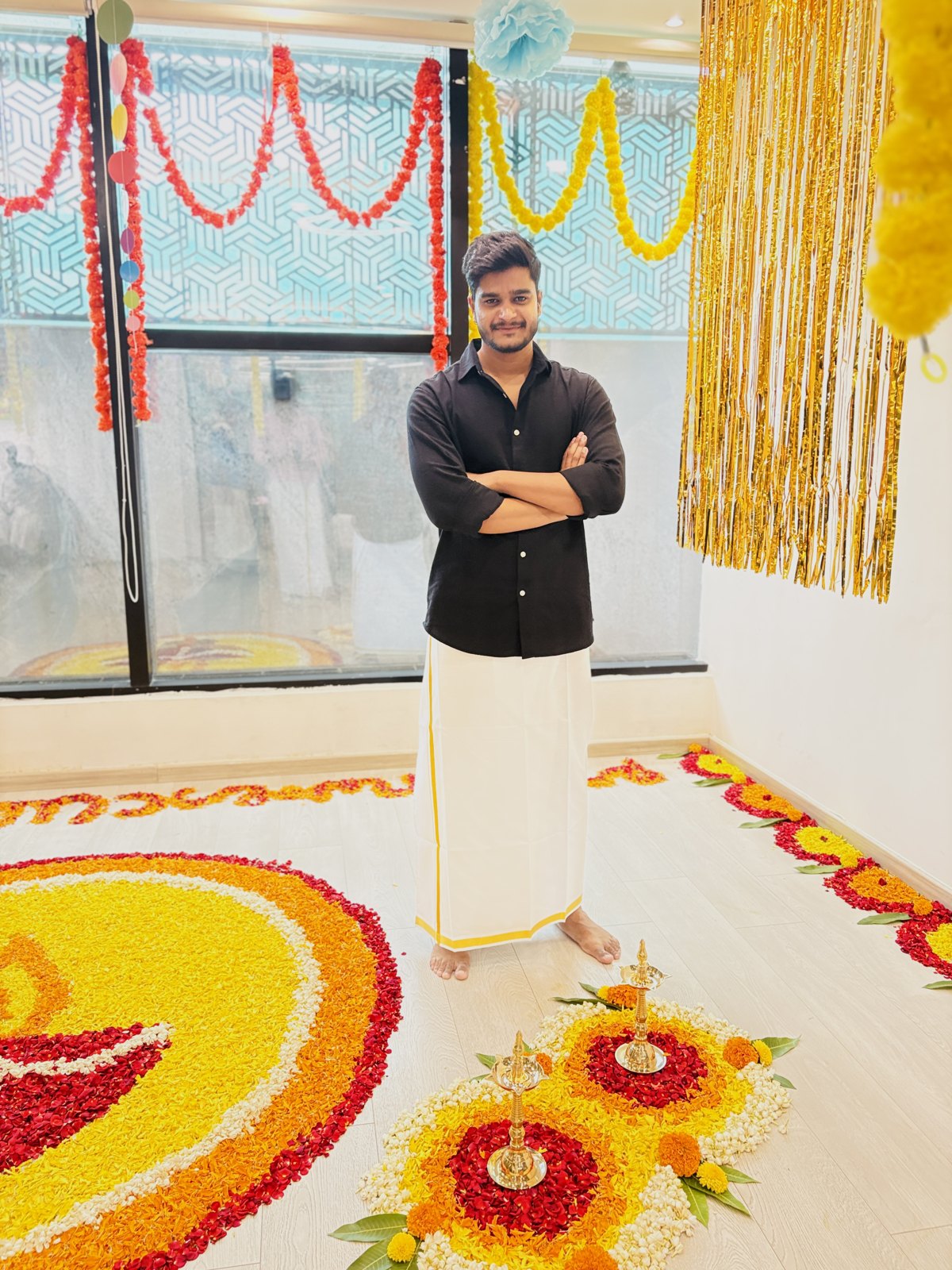 Sanskar Shivhare in a black shirt and traditional white attire at a celebration with floral decorations